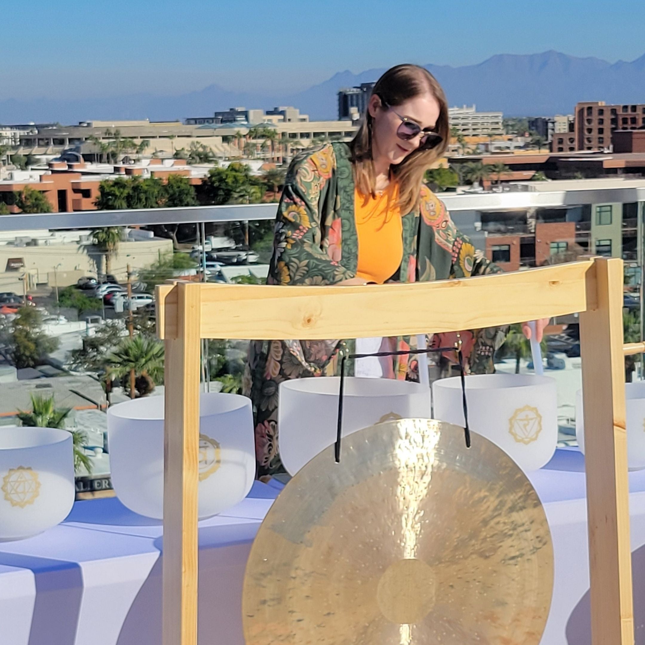 Liz playing a large gong on a rooftop with Scottsdale cityscape in the background
