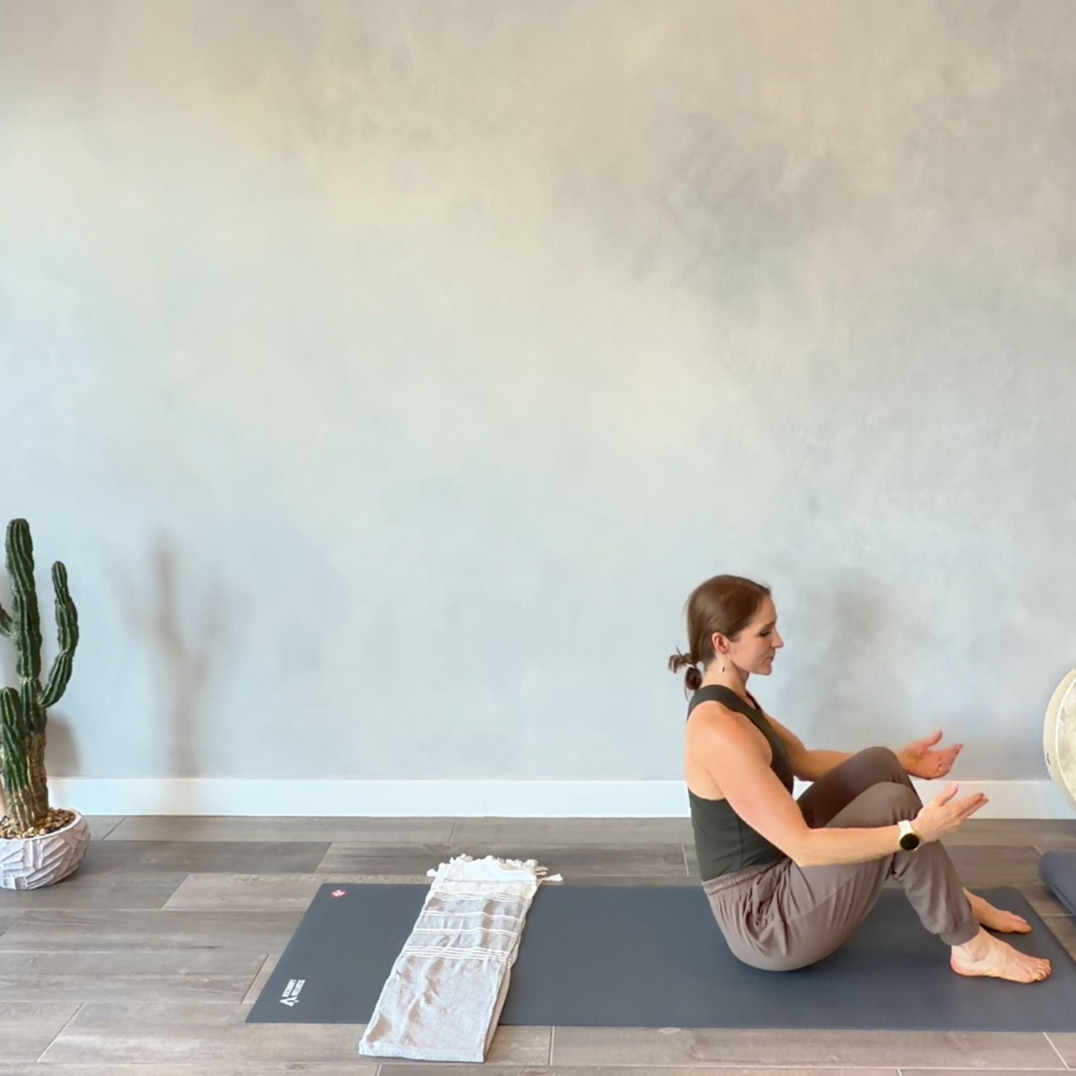 Woman practicing yoga in a studio with a cactus plant and an elegant concrete wall in the background.