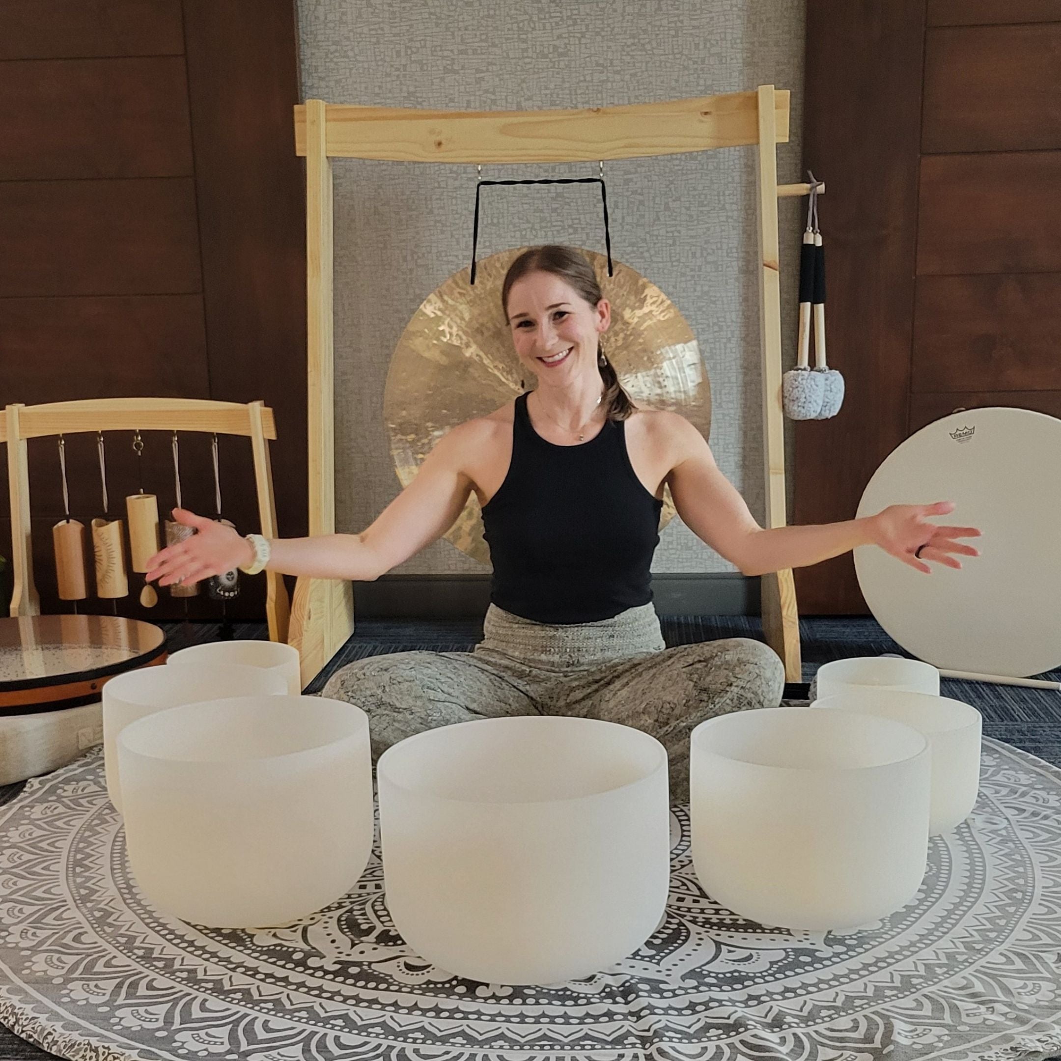 Founder Liz Adriano welcoming everyone with white bowls in a room with sound meditation instruments