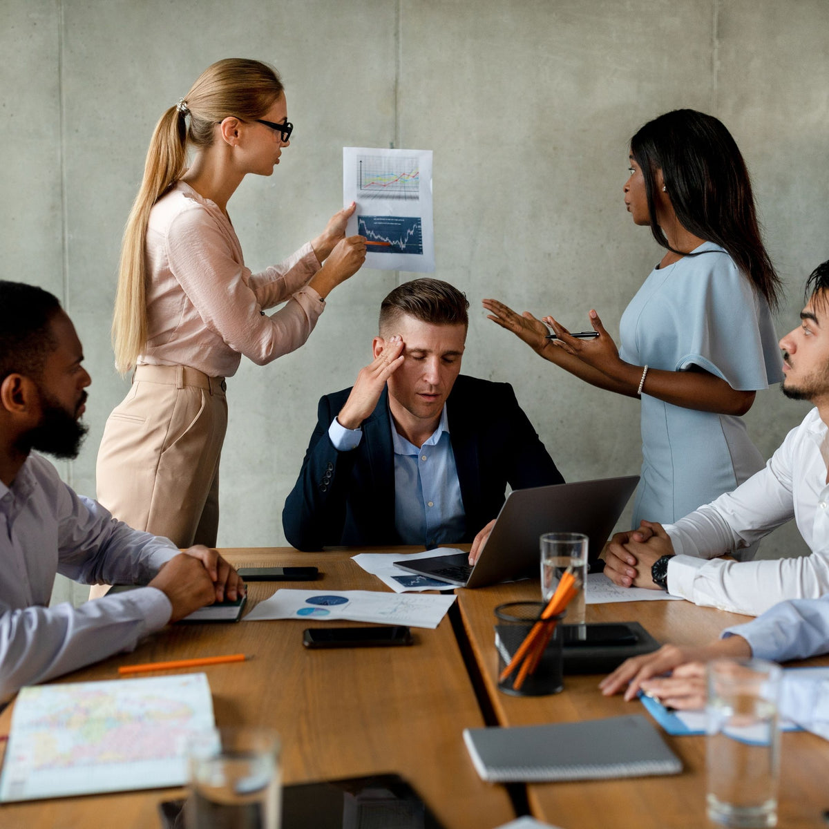 Group of stressed executives in a meeting around a table with documents and laptops.