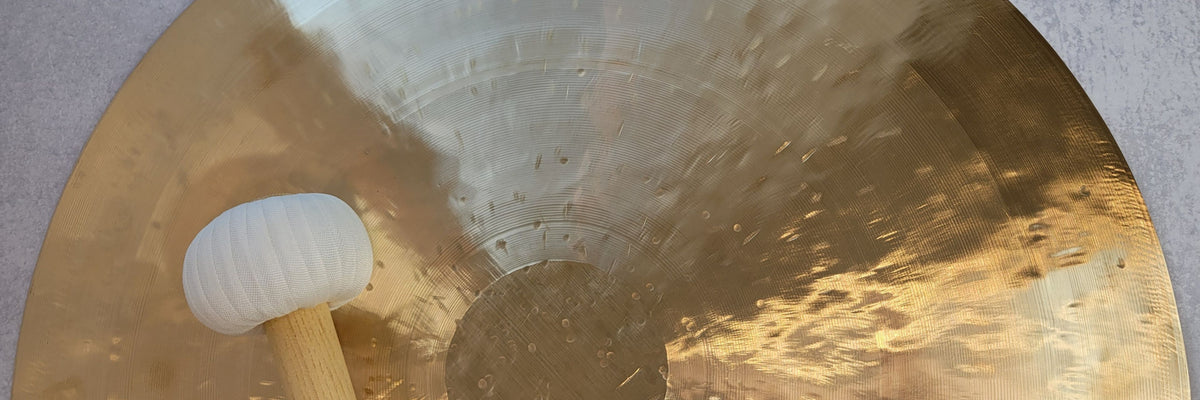 Close-up of a large gong with a mallet on a textured surface.