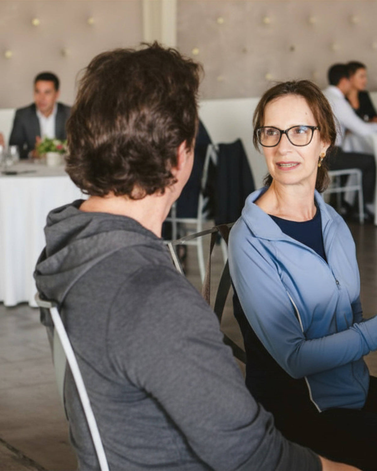 Two leaders sitting at a table having a discussion in a formal setting with other attendees in the background of a Colorado Ascendify Wellness Interactive Keynote.