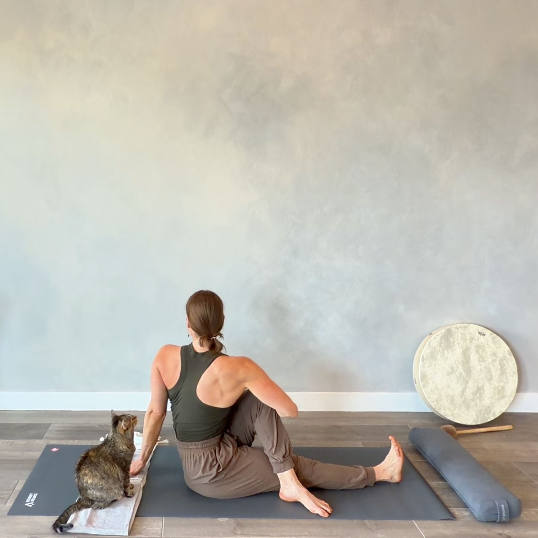 Person sitting on a yoga mat with a cat and a meditation drum in an elegant studio.