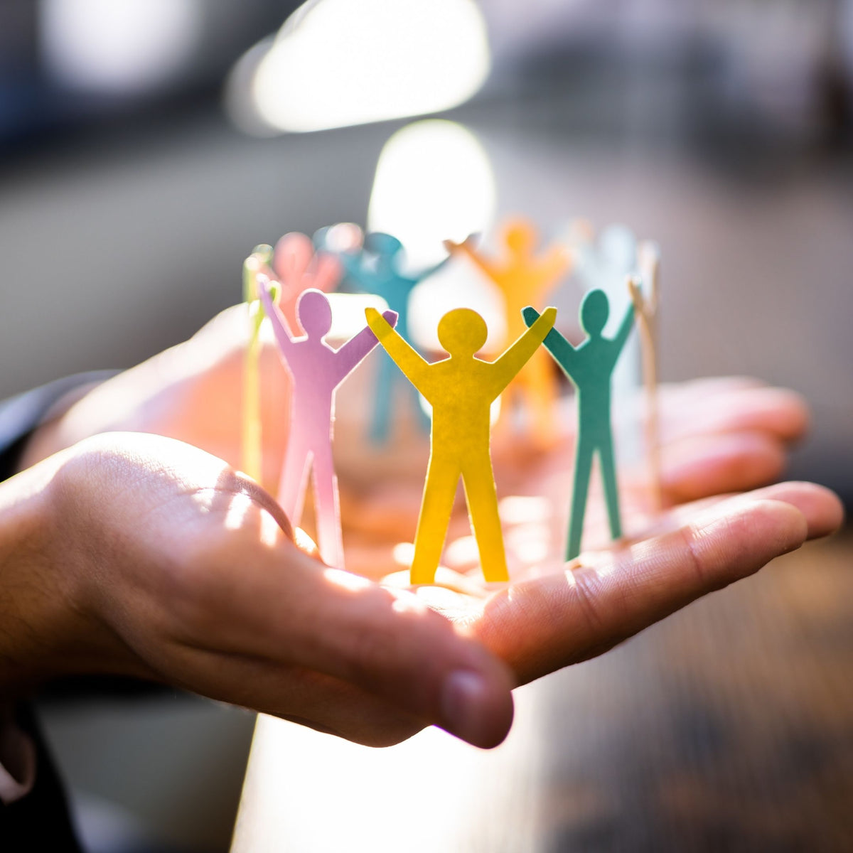 Colorful paper cutout figures of people held in a hand with a blurred background