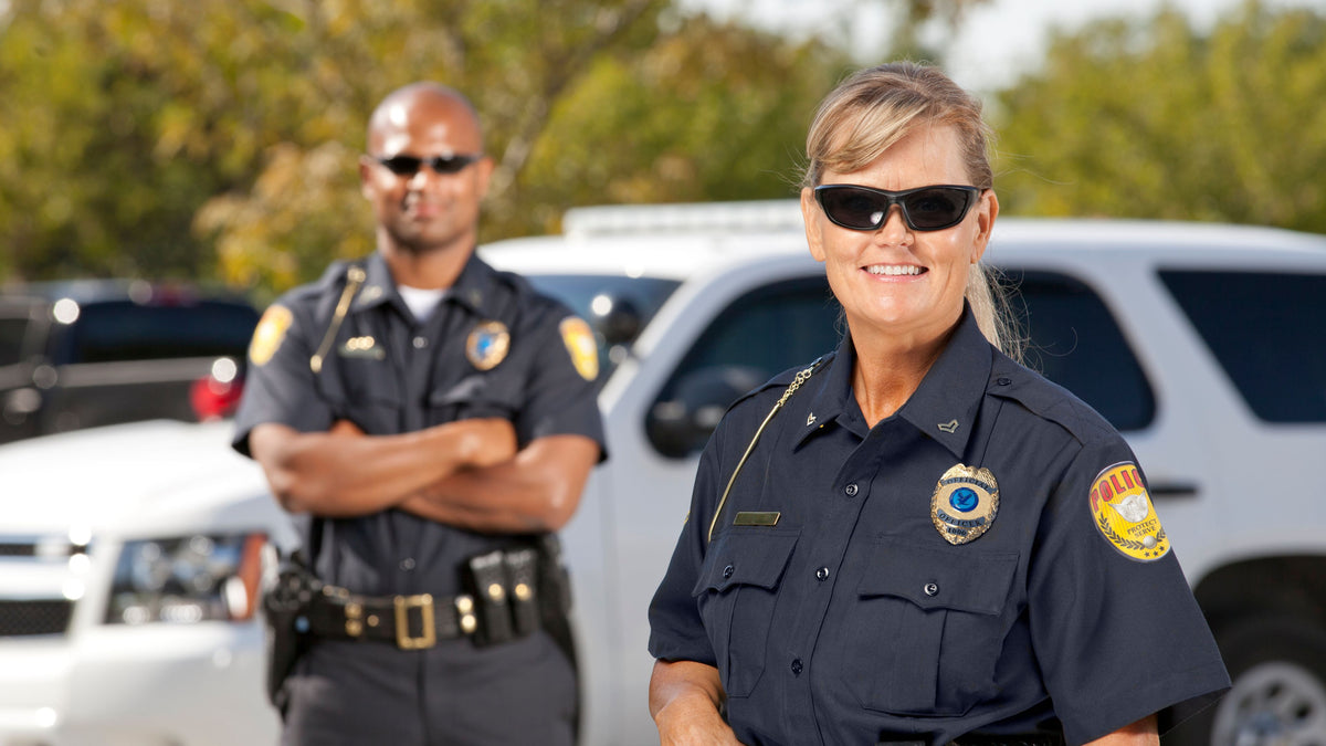 Two police officers standing in front of a vehicle with trees in the background