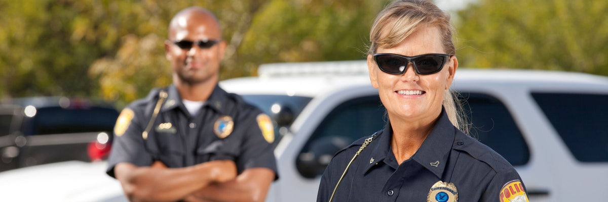 Two police officers standing in front of a vehicle with trees in the background