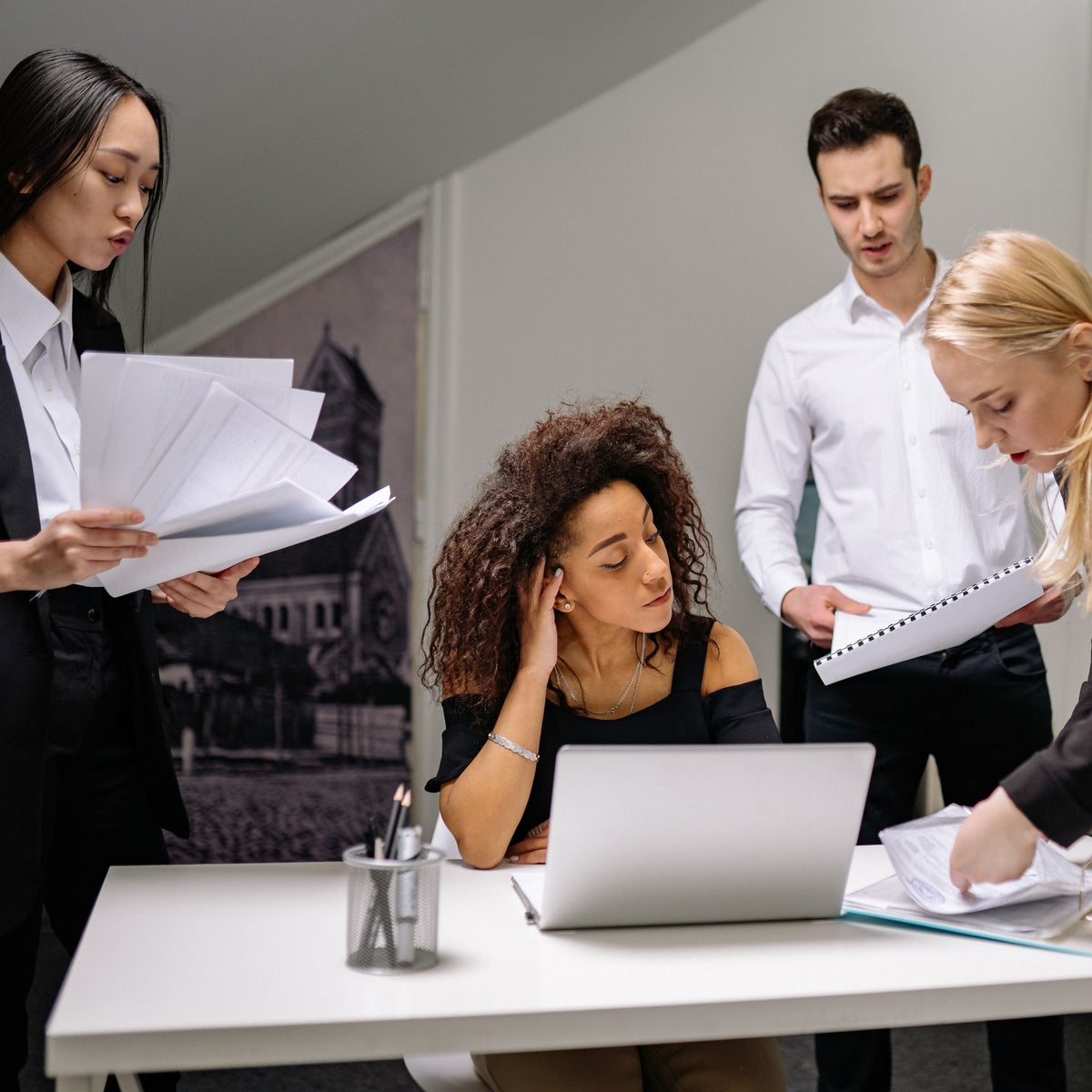 Group of stressed entrepreneurs working together in an office setting with a laptop and documents.